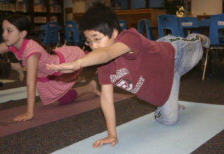 Fifth-graders Joan Hui Kim and Maddy Deroche practice a yoga stretch during class at Nautilus Elementary School on Monday.