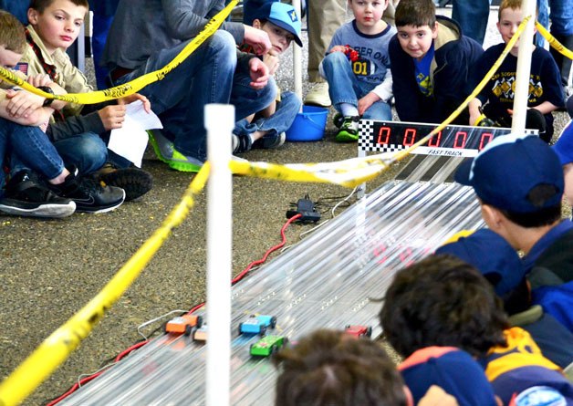 Cub Scouts watch as wooden race cars speed down an aluminum track over the electronic finish line during the finals of the Hylebos District
