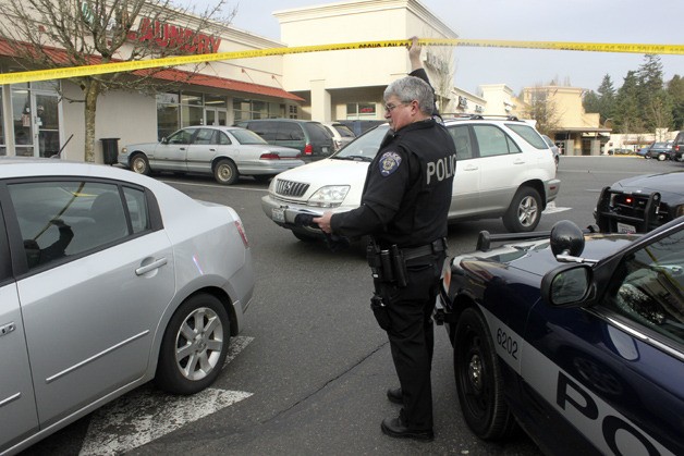 A Federal Way police officer lifts up the crime scene ribbon so vehicles can exit the Dash Point Village shopping center following a shooting Friday afternoon near the Starbucks on SW Dash Point Road.
