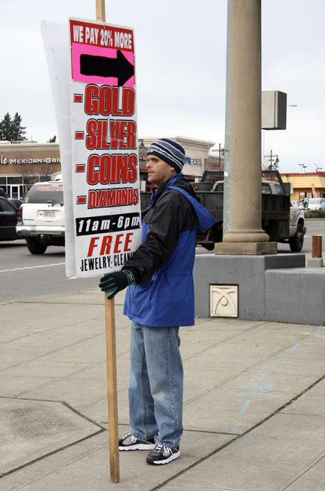 Ryan Vanderlinda held a sign on Friday at the corner of 320th Street and Pacific Highway South advertising the services of Federal Way’s American Gold Inc. The business buys precious metals. The city council is considering stricter regulation of businesses that buy jewelry