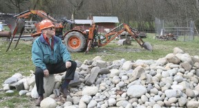 Donald Barovic sits on a pile of rocks he removed from his soil. Barovic's goats can be seen in the background.