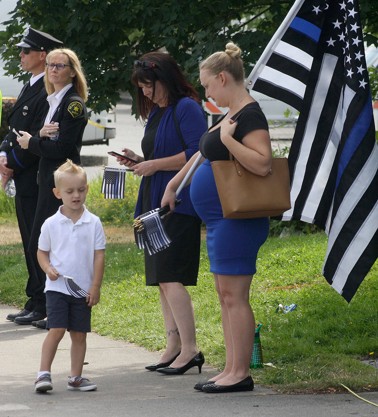 A woman brings a large flag and small flags as she watches the procession Tuesday for Kent Police Officer Diego Moreno along West James Street. STEVE HUNTER, Kent Reporter