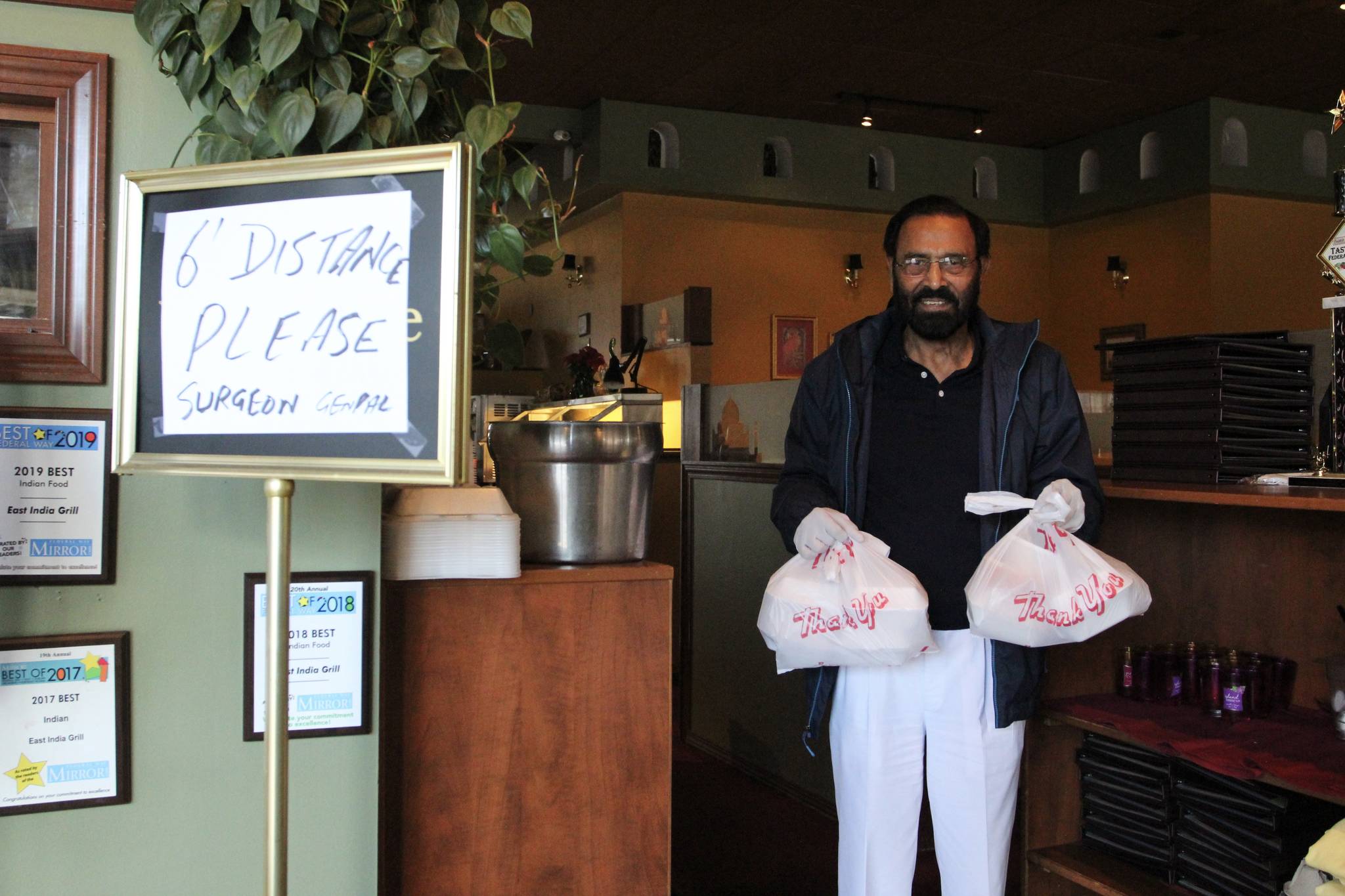 Kabal Gill, owner of East India Grill, wears gloves to hand over take-out orders at his restaurant on March 23, 2020. Olivia Sullivan/staff photo