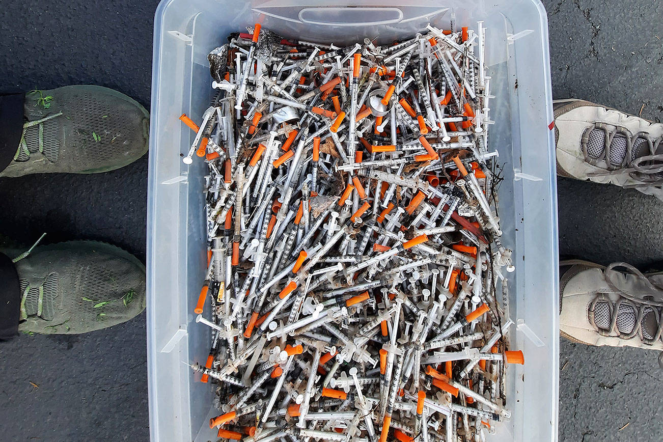 Federal Way residents David Zumwalt, left, and Grace Lubrano stand over a bin of needles and a bucket of trash collected from encampments in the West Hylebos Wetlands Park in Federal Way on May 10. Photo courtesy of Grace Lubrano