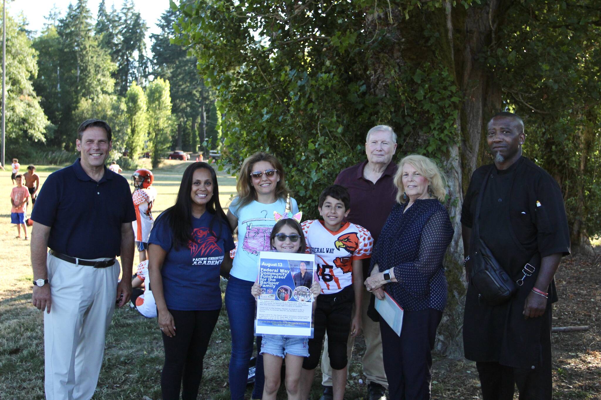 Marwa Almasri, center in blue, accepted a $1,000 donation on behalf of Jay Barbour on Aug. 16. The donation funds were collected by community donations and a portion of sales from K.C. Deez BBQ. From left: Mayor Jim Ferrell; Eileen Wilson of Pacific Christian Academy; Marwa Almasri and her daughter, Nai Barbour and her son, Majed Barbour; Rose Ehl of the Federal Way Farmers Market and her husband, Dave; and K.C. Deez BBQ owner De Davis. Olivia Sullivan/the Mirror