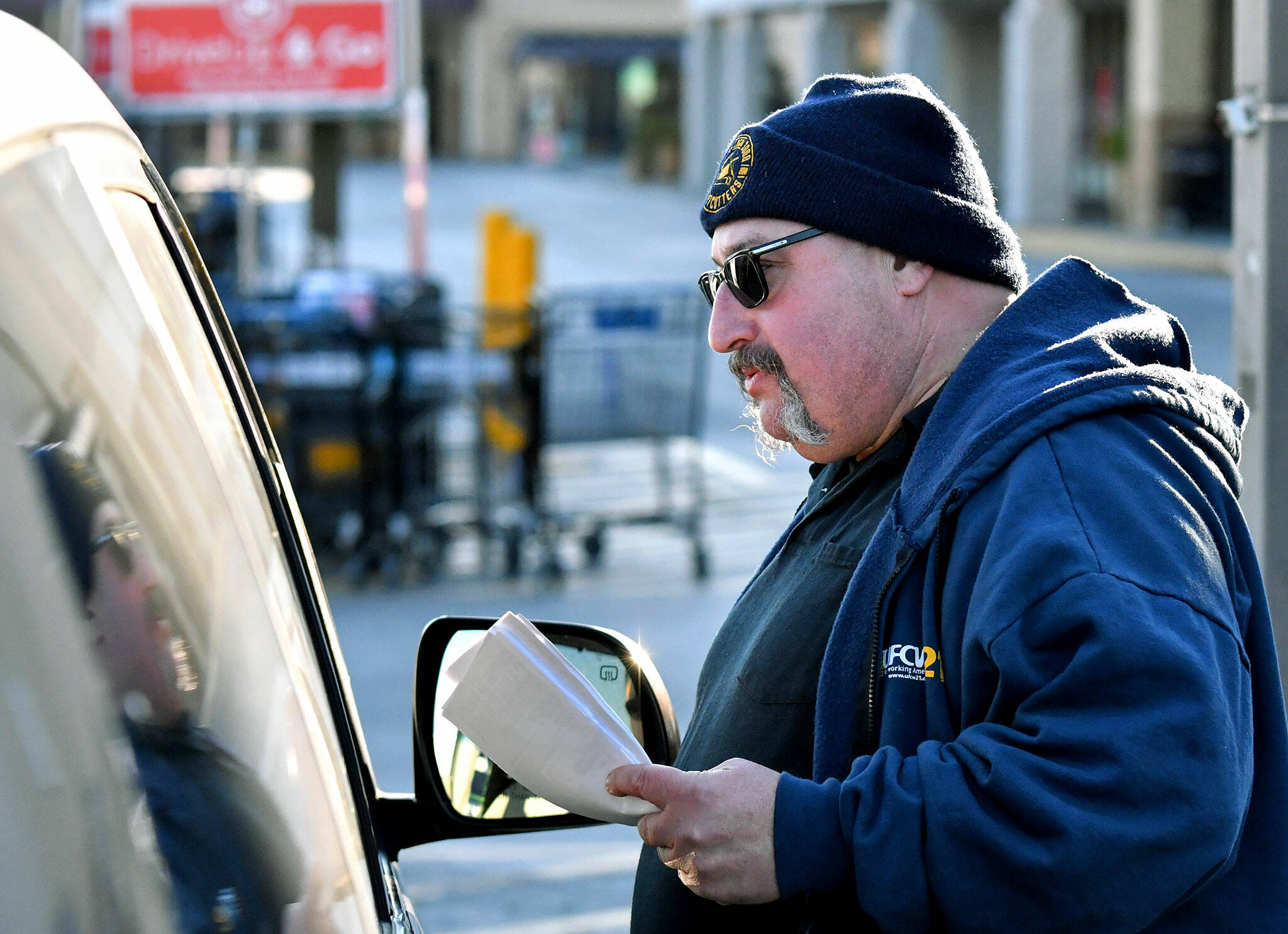 Kevin Flynn, a meat-cutter with the Marysville Albertsons, speaks with a passenger in a vehicle during a leaflet campaign on Wednesday. Flynn was one of about a dozen grocery store workers handing out leaflets to shoppers about the proposed merger between Albertsons and Kroger. (Mike Henneke / The Herald)