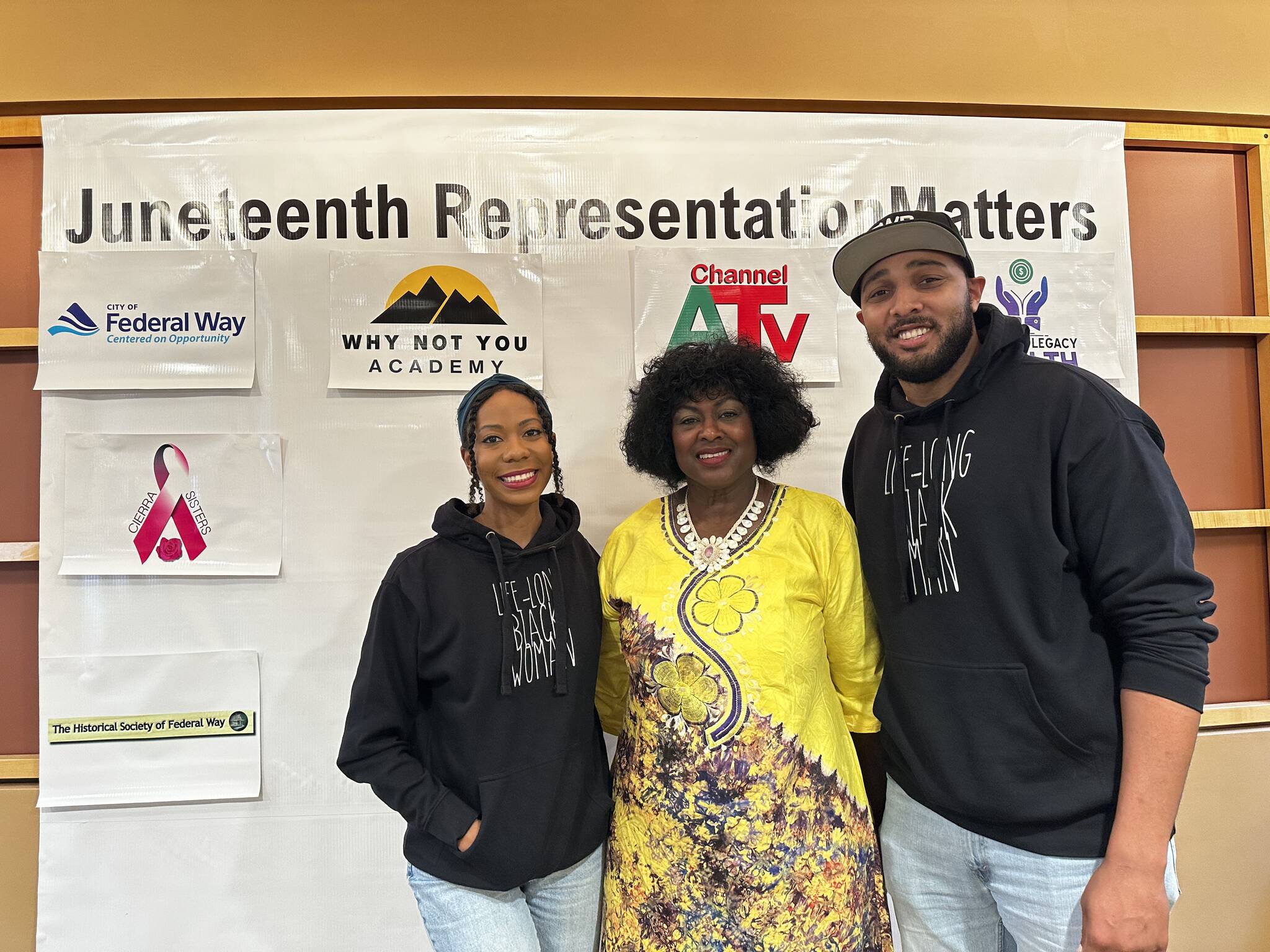 Marlie Love, Tirzah Idahosa and Anthony Love pose for a picture together in front of the Juneteenth event sponsors. (Photo by Joshua Solorzano/The Mirror)