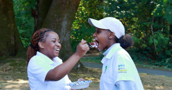 Photo by Keelin Everly-Lang / The Mirror
Youth Director Fiona Okech does the honors of feeding the birthday girl her first bite. Fiona and Sharlene went to school together in Kenya 9 years ago and the two friends were reunited here in South King County this year when their mothers reconnected.