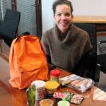 Valerie Danforth, the organizer of the Bridging A Gap Weekend Feeding Program, sits with a backpack and the food it contains, an example of what children take home each weekend in the program. RAECHEL DAWSON, the Mirror