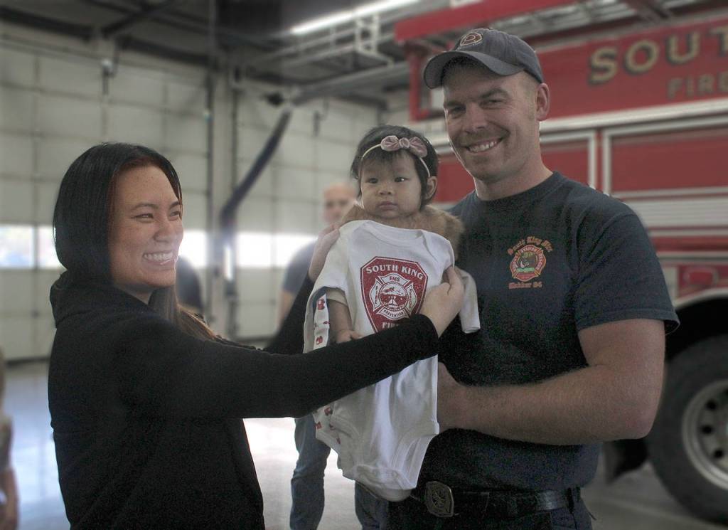 South King Fire & Rescue firefighter/EMT Randy White holds 7-month-old Kylie Kuo while her mother, Diane Kuo, holds a SKFR onesie specially made for Kylie up in front of her at a special reception Monday at Station 62 in Federal Way. White was one of the first responders who helped deliver Kylie April 6. JESSICA KELLER, the Mirror