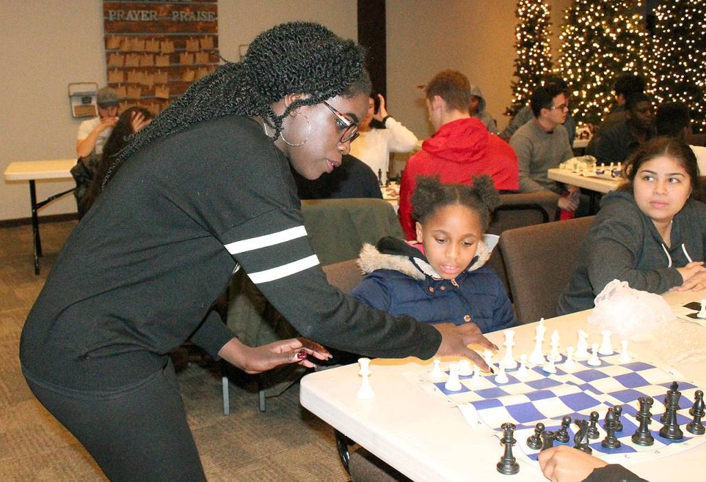 Phiona Mutesi, an international chess champion from Uganda who was depicted in a movie Queen of Katwe, helps 10-year-old Thalia Smith arrange the chess board as 13-year-old Samantha Valenzuela looks on during a Chess with the Superintendent session Wednesday at Family Life Community Church. The youth, most of whom are students in Federal Way, received a basic lesson from Superintendent Tammy Campbell, while Mutesi walked around offering pointers to students. The students left with a chess board of their own. JESSICA KELLER, the Mirror