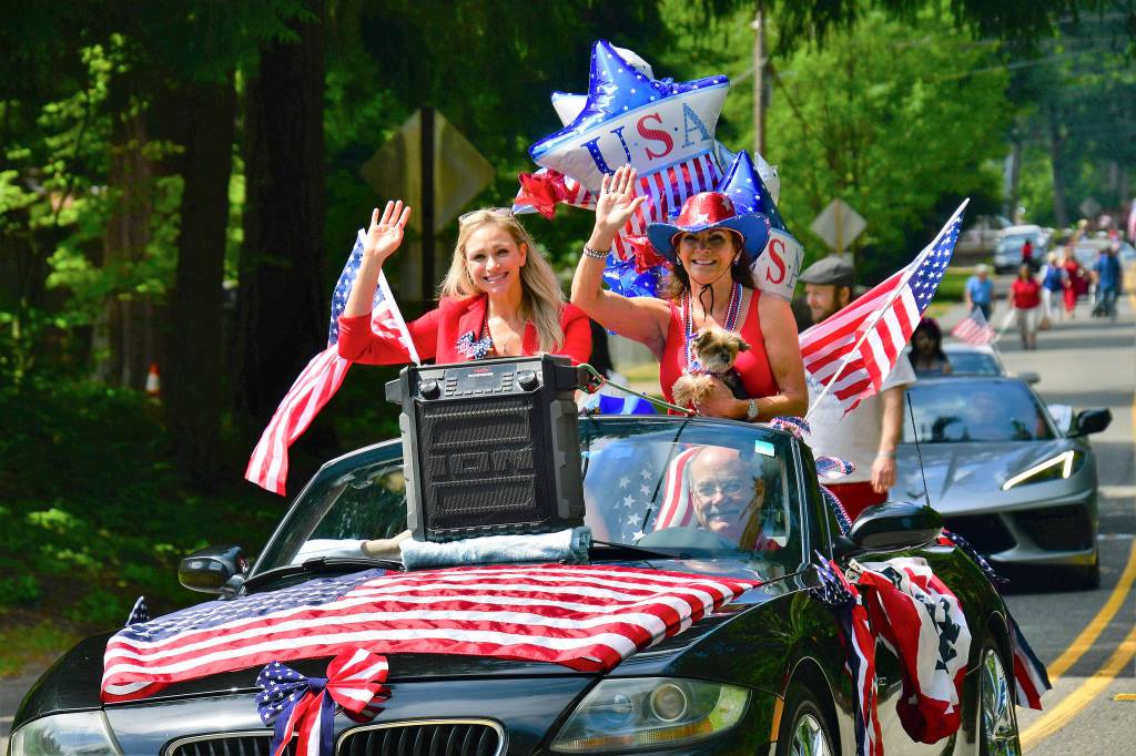Two women wave from a Fourth of July float. Photo by Bruce Honda