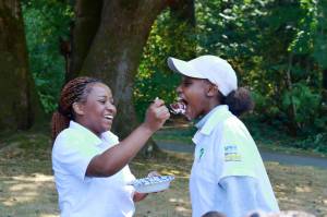 Photo by Keelin Everly-Lang / The Mirror
Youth Director Fiona Okech does the honors of feeding the birthday girl her first bite. Fiona and Sharlene went to school together in Kenya 9 years ago and the two friends were reunited here in South King County this year when their mothers reconnected.