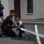 Giovanni Bonilla, a Zone 3 Fire Cadet with a young boy shooting the fire hose at targets at the South King Fire 75th anniversary.