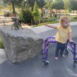 A child with a walker points to a fun statue of an animal using a walker at the Chelsea Anderson Memorial Play Station (CHAMPS) @Marshall Park in Vancouver, Washington. Photo from Harpers Park, the organization that designed, funded and provided construction oversight for the playground. Concept design for the park was by Todd Girvin of Harpers Playground.