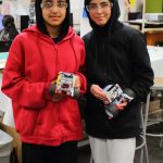 Two students at Kilo Middle School show off their robots that they are working on programming to circle a table and stop at a specific point. Photo by Keelin Everly-Lang / the Mirror