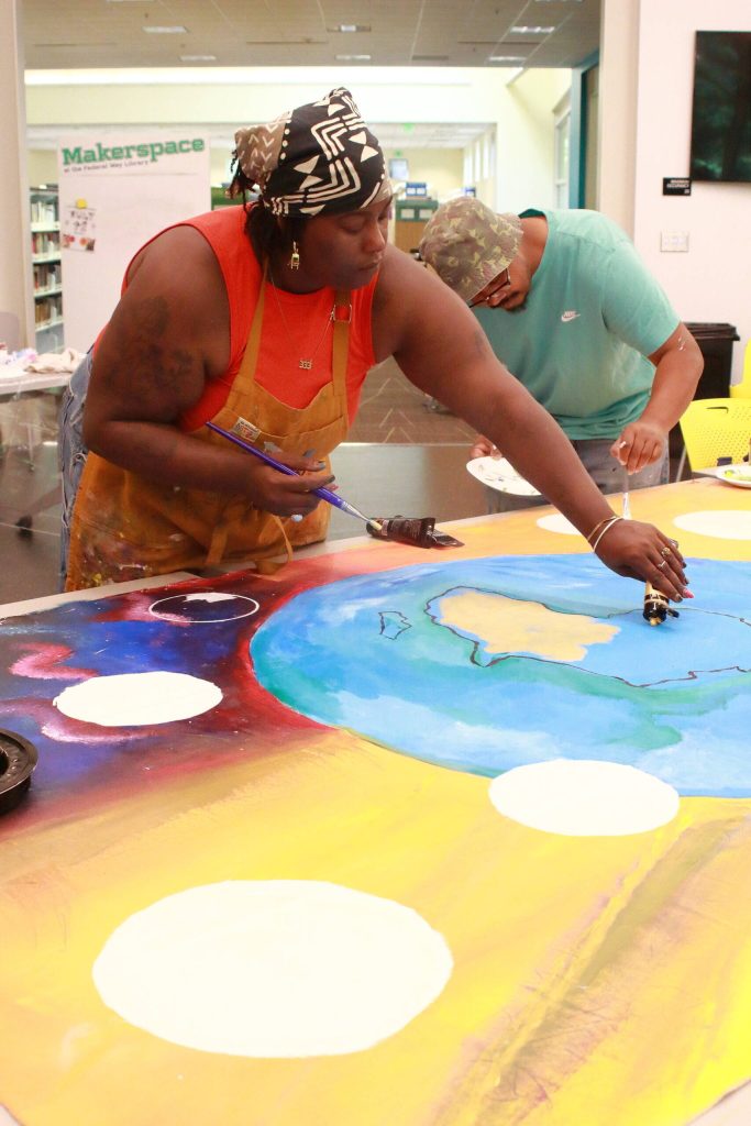 Deycha Nhtae works on the community mural at Saturdays Juneteenth event. Photo by Keelin Everly-Lang / the Mirror.