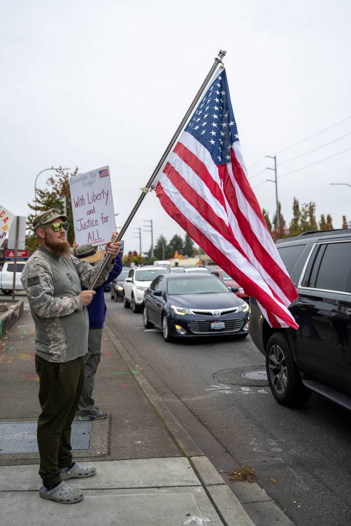American flags and expressions of love for the country were everywhere at the No Kings protest, like this individual wearing a U.S. Army shirt and holding an American flag. The protest took place on S. 320th Street, which has the honorary name Veterans Way. Behind him is someone holding a sign stating Remember your pledge? With liberty and justice for ALL. Many signs included messages of opposition to the current administration and overreaches of constitutional authority. Photo by Rachel Jones