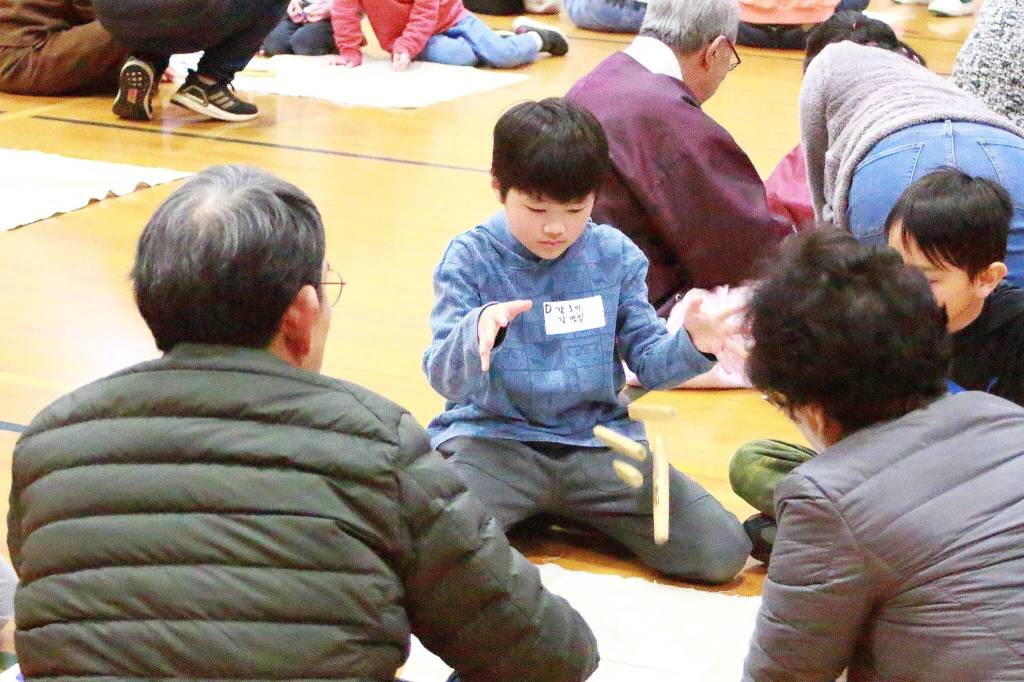 Multiple generations play yut nori together, a board game played at New Years. Photos by Keelin Everly-Lang / the Mirror